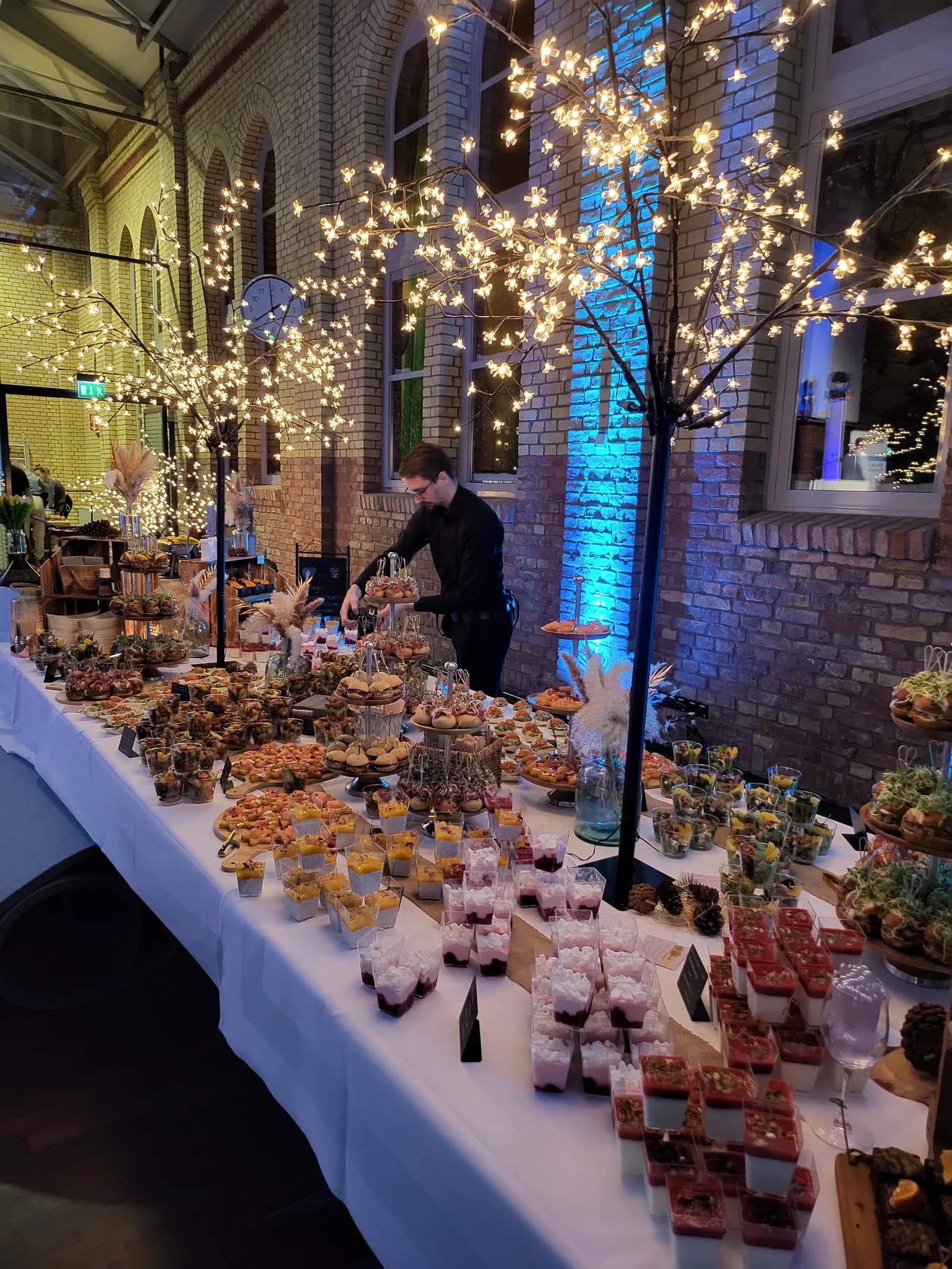 Festlich gedeckter Catering-Tisch mit Fingerfood unter blühenden Lichterbäumen bei einer Abendveranstaltung