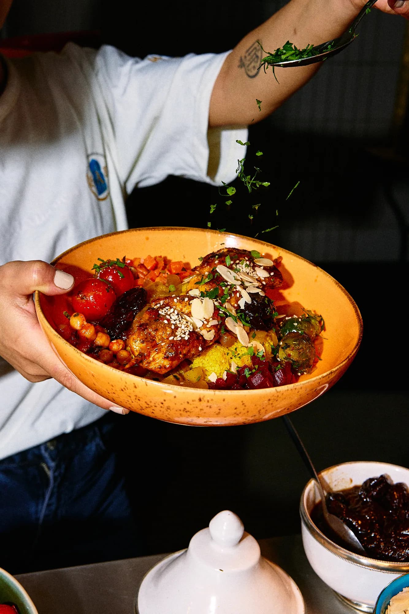 Frische Kräuter werden über eine Bowl mit Hähnchen-Tajine, Couscous und Gemüse gestreut