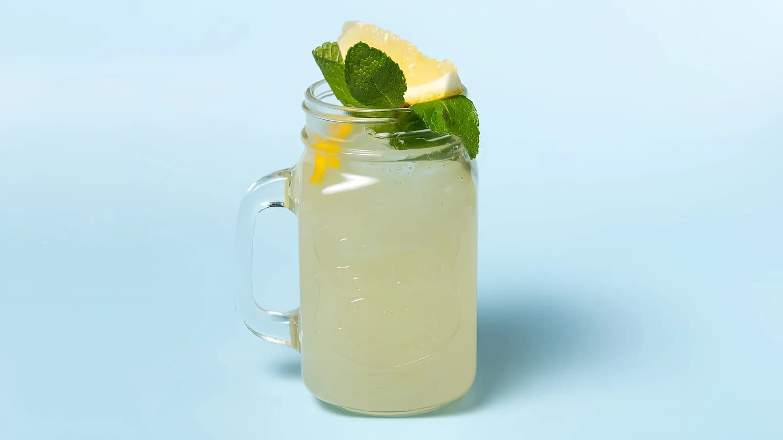 Homemade lemon lemonade in a handled jar with lemon and mint