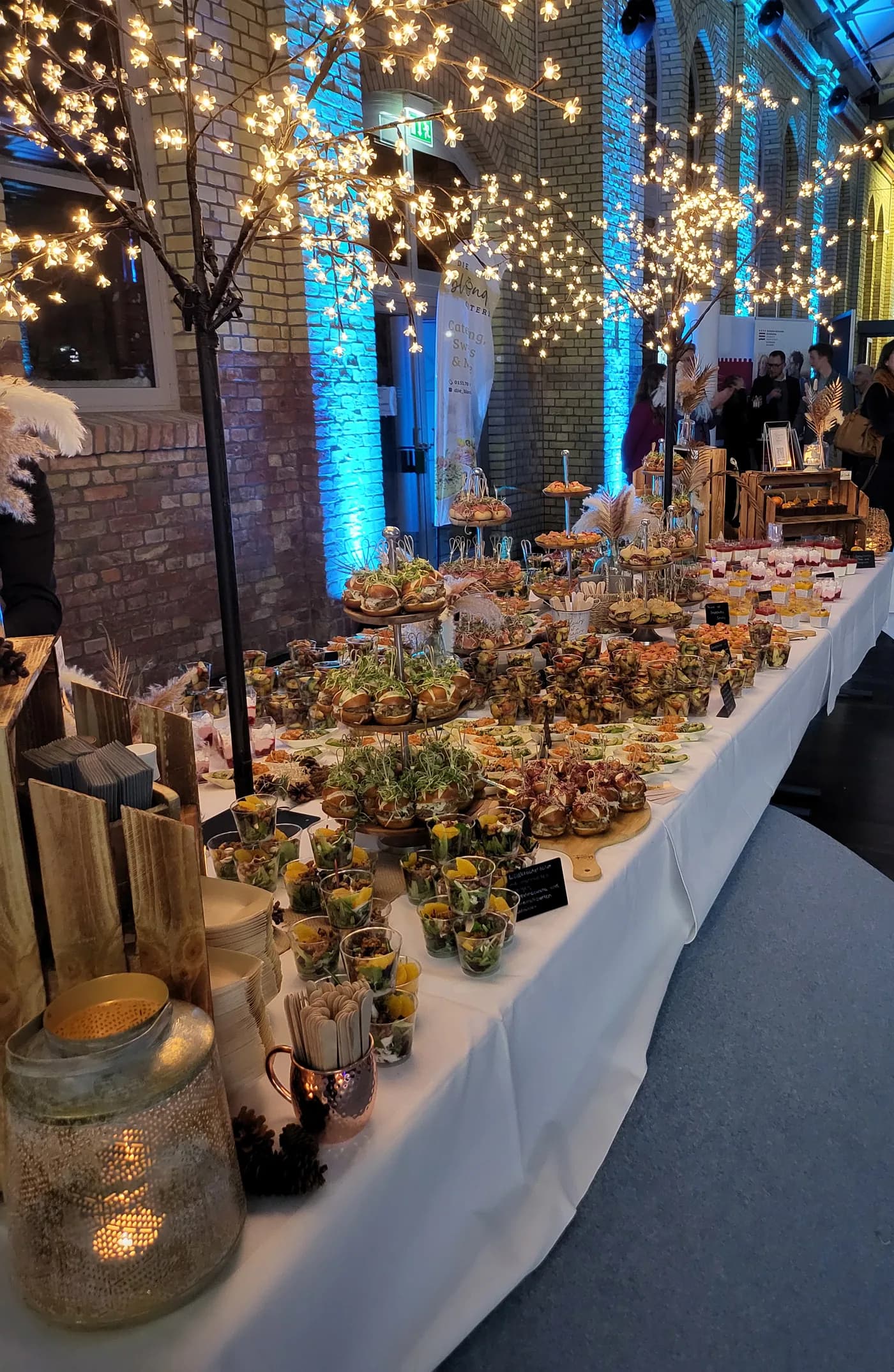 A long buffet table of canapés and desserts under lit trees at a corporate event